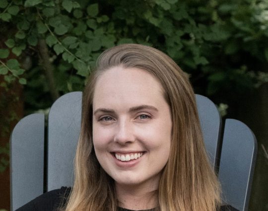 Grace Melcher sitting in Adirondack chair with trees in the background