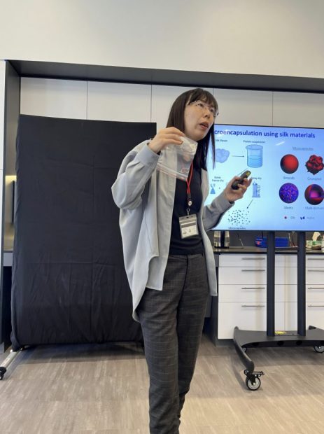 A woman standing in front of a presentation screen, holding up a plastic bag